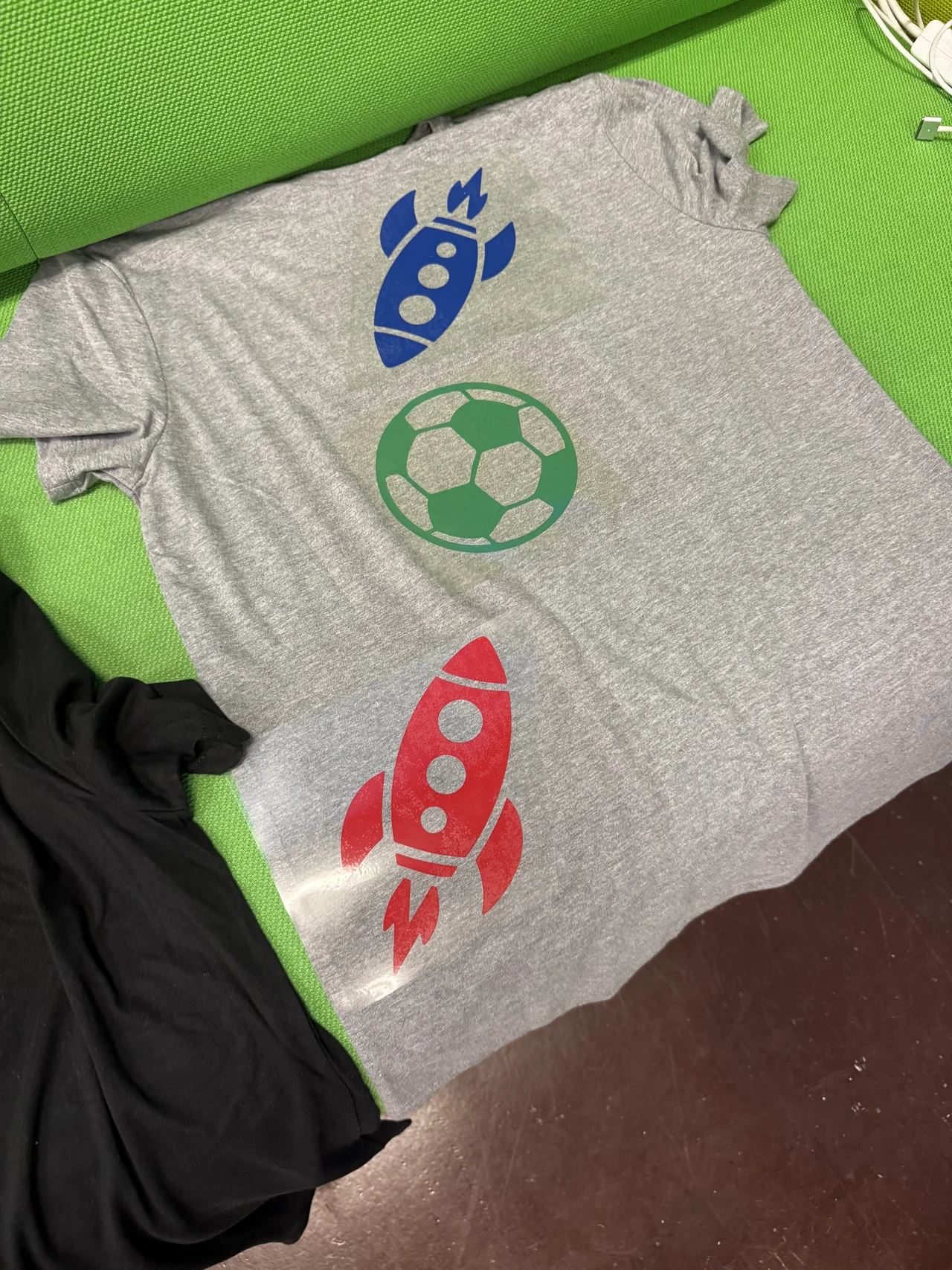 A finished gray shirt with a blue rocket, green soccer ball and red rocket design.