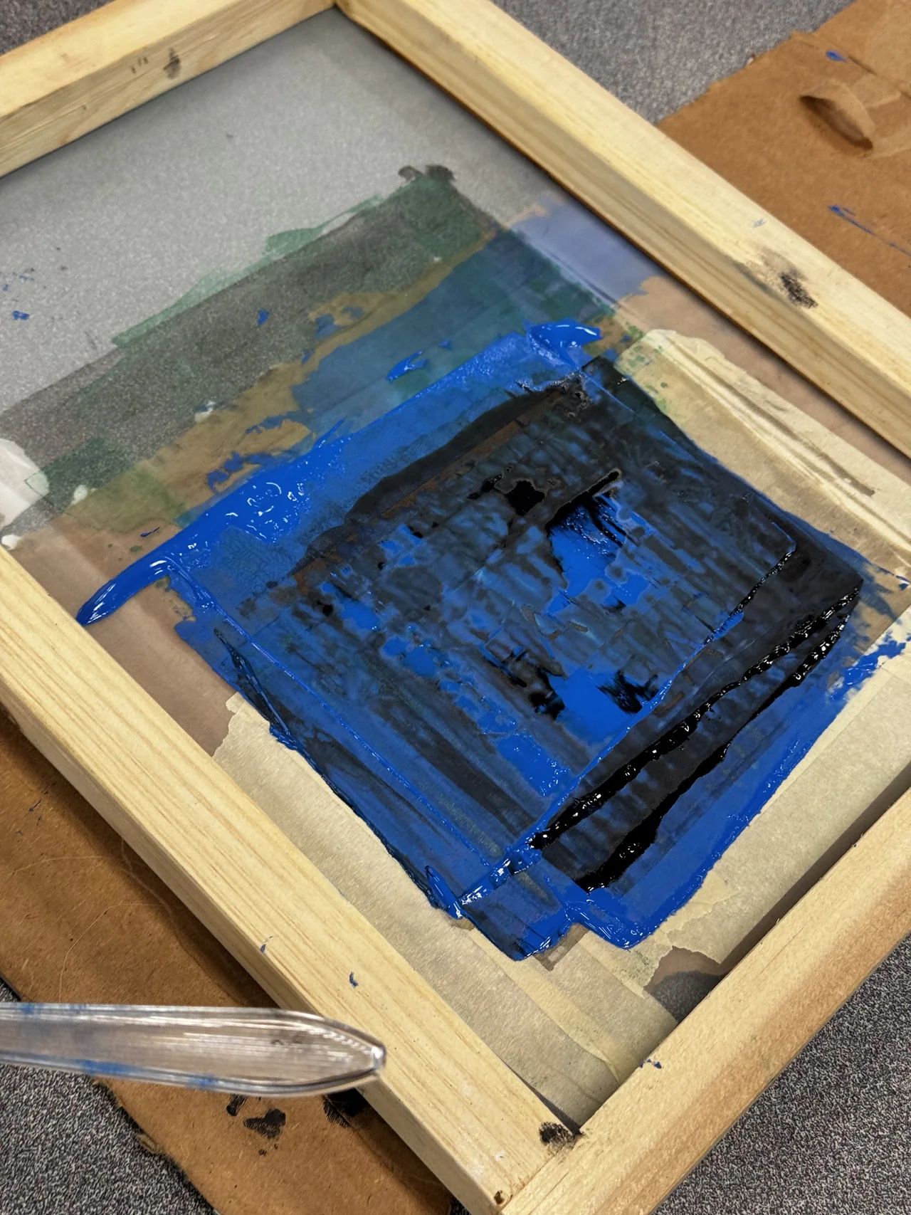 A wooden screen-printing frame with blue ink and a squeegee on the work table.