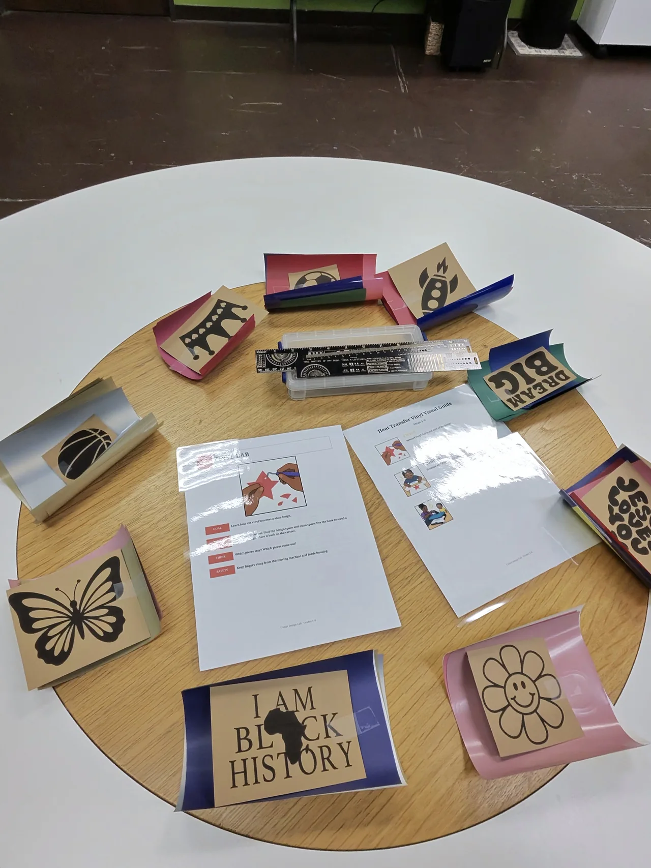 A work table set with colored vinyl, design stencils and illustrated heat-transfer instructions.