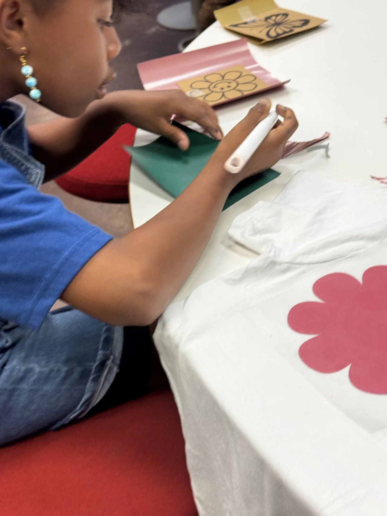 A student carefully removes small pieces from a vinyl design beside a white shirt with a pink flower.